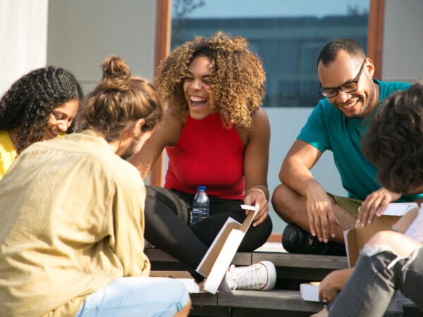 Happy joyful friends talking and laughing Happy joyful friends talking and laughing over outdoor lunch. Mix raced group of young people sitting on outdoor stairs and eating takeaway pizza from box. Mealtime outside concept
